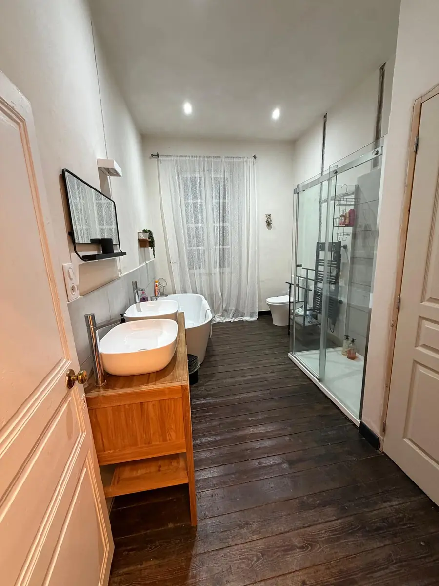The main bathroom: twin basins on a wooden vanity, a freestanding bath under a long sheer curtain, and a large glass shower enclosure, on dark wooden floorboards