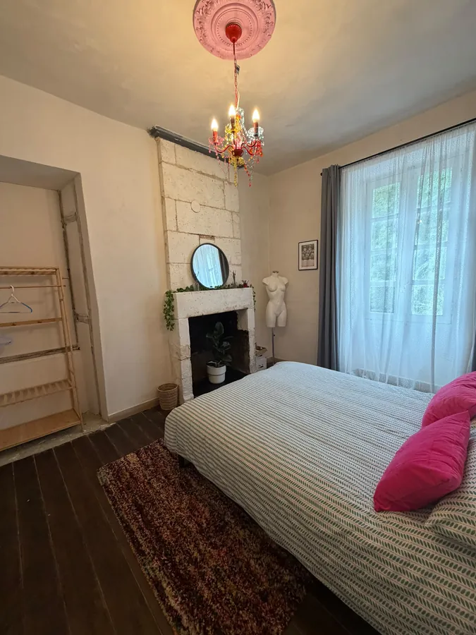 The stone fireplace in Bedroom Two with a round mirror above it, trailing ivy and a plant in the hearth