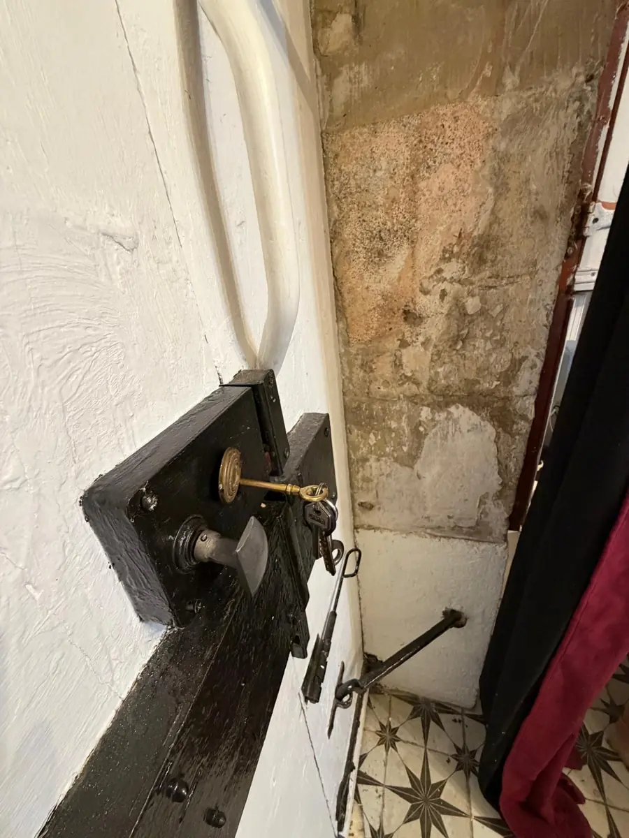 The inside of the front door: a black box lock with a brass key, and the bolt below it, above the star-tiled hall floor