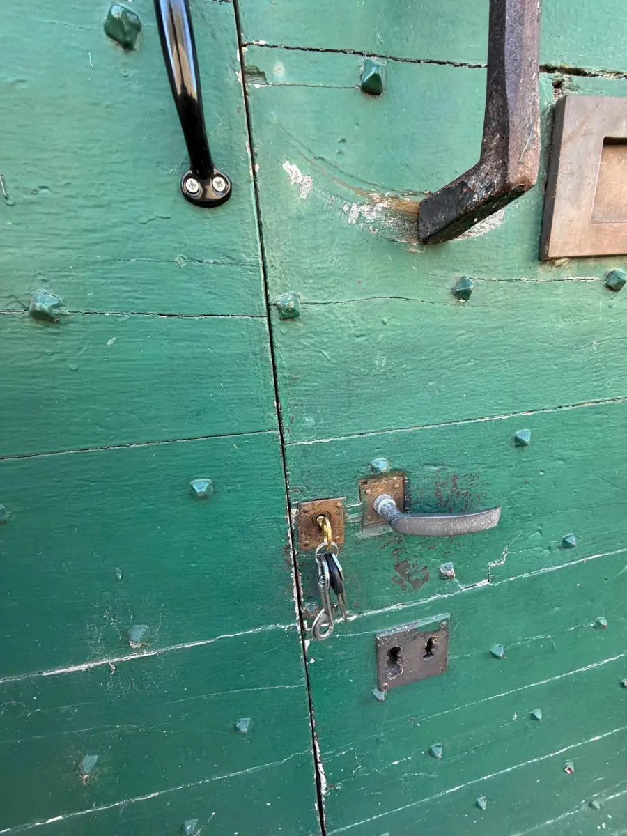 The two leaves of the green studded door from outside, with the key in the lock and the lever handle beside it