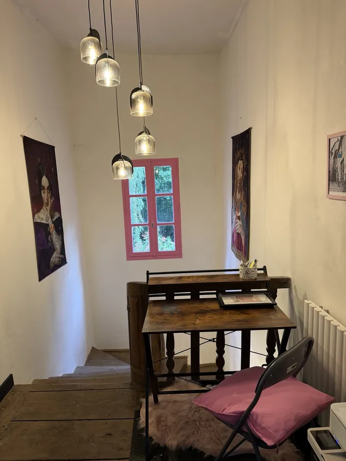 A wooden table and folding chair with a pink cushion on the landing, beneath a cluster of glass pendant lights