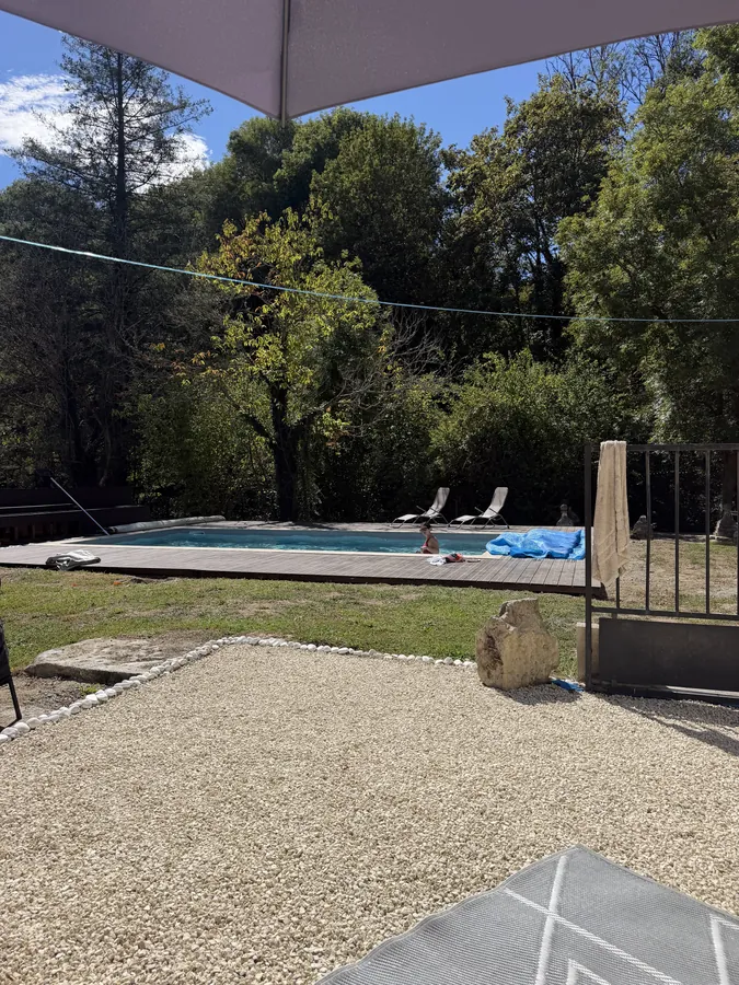 The pool area from the side, cover on, with loungers, gravel and the garden trees behind