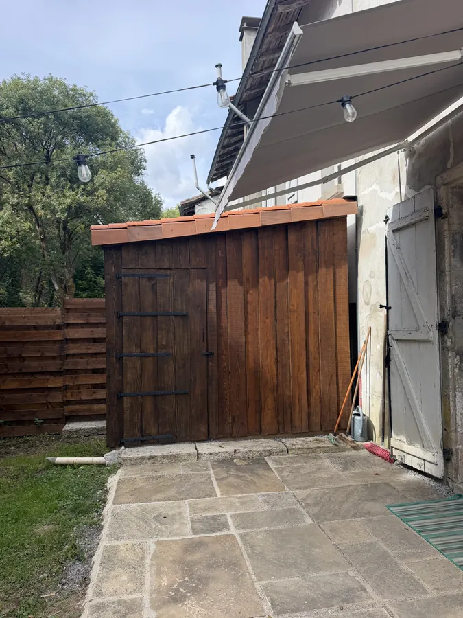 The timber door of the outdoor bathroom in the corner of a stone-paved yard, under an awning