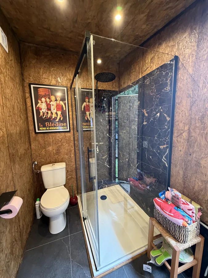 Inside the outdoor bathroom: a walk-in shower behind glass beside a toilet, with boarded walls