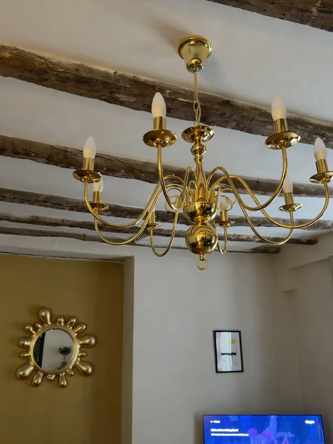 A polished brass chandelier hanging from dark timber beams, with a gilded sunburst mirror on the wall below