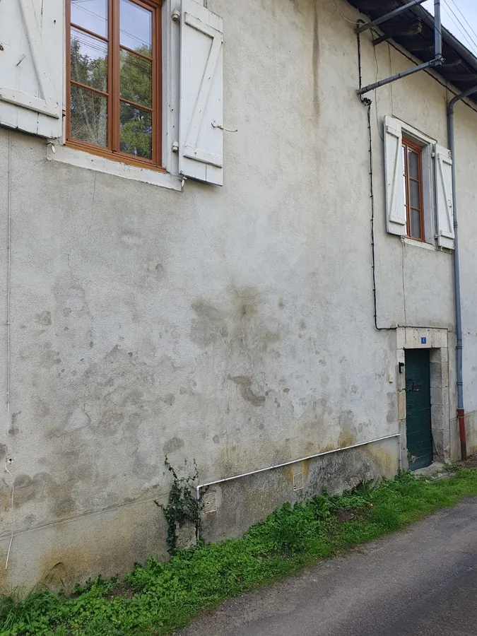 The side wall of the house on the lane, with shuttered windows and a dark green door at the far end