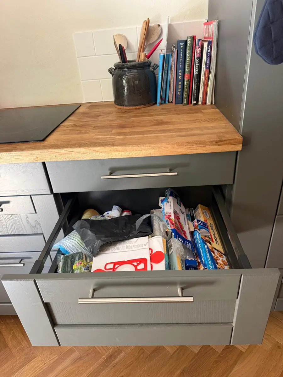 A deep grey kitchen drawer pulled open beneath the wooden worktop and hob, holding rolls of bin bags