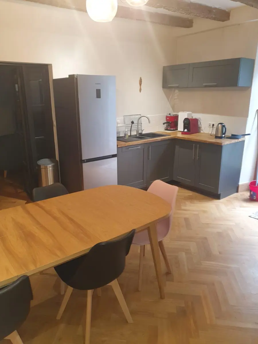 The kitchen: grey fitted units with wooden worktops, a tall fridge-freezer, and an oval wooden dining table with grey and pink chairs on a herringbone floor