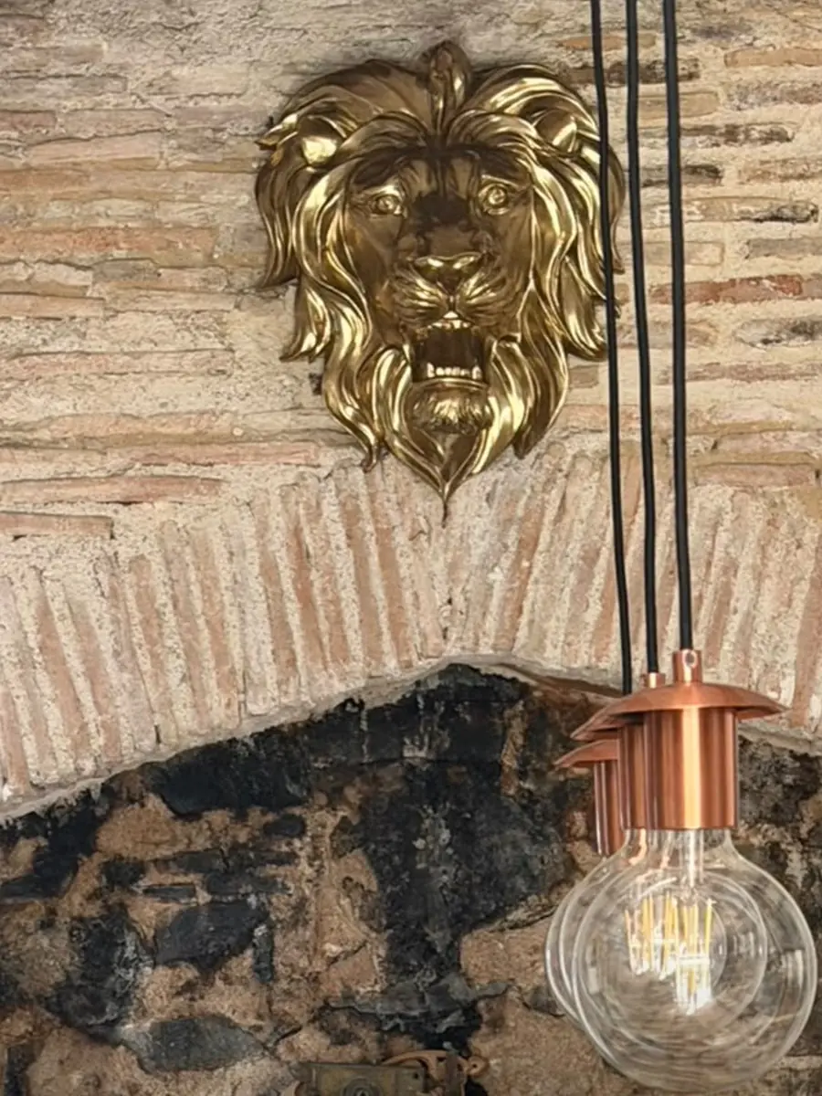 A gold lion&rsquo;s head on the old stone and brick fireplace opening, with copper pendant lights hanging in front of it