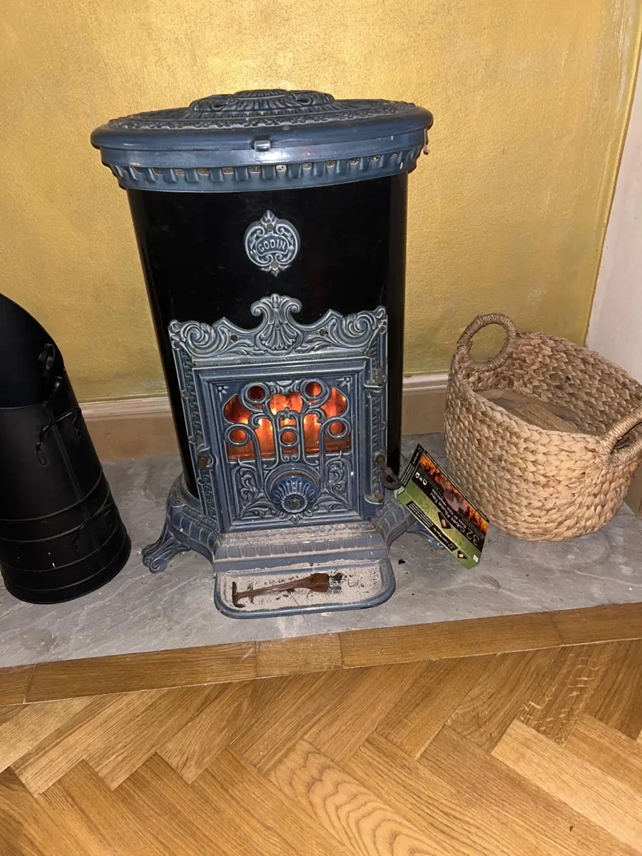 Close-up of the black and silver enamelled wood burner on its stone hearth, beside a woven log basket