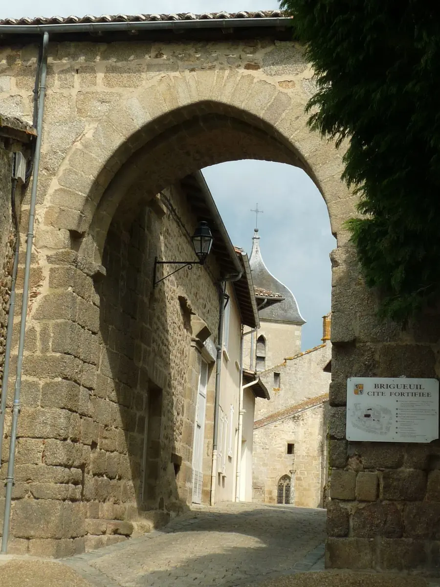 A stone gateway arch in Brigueuil, looking through to an old street of stone houses and the church spire