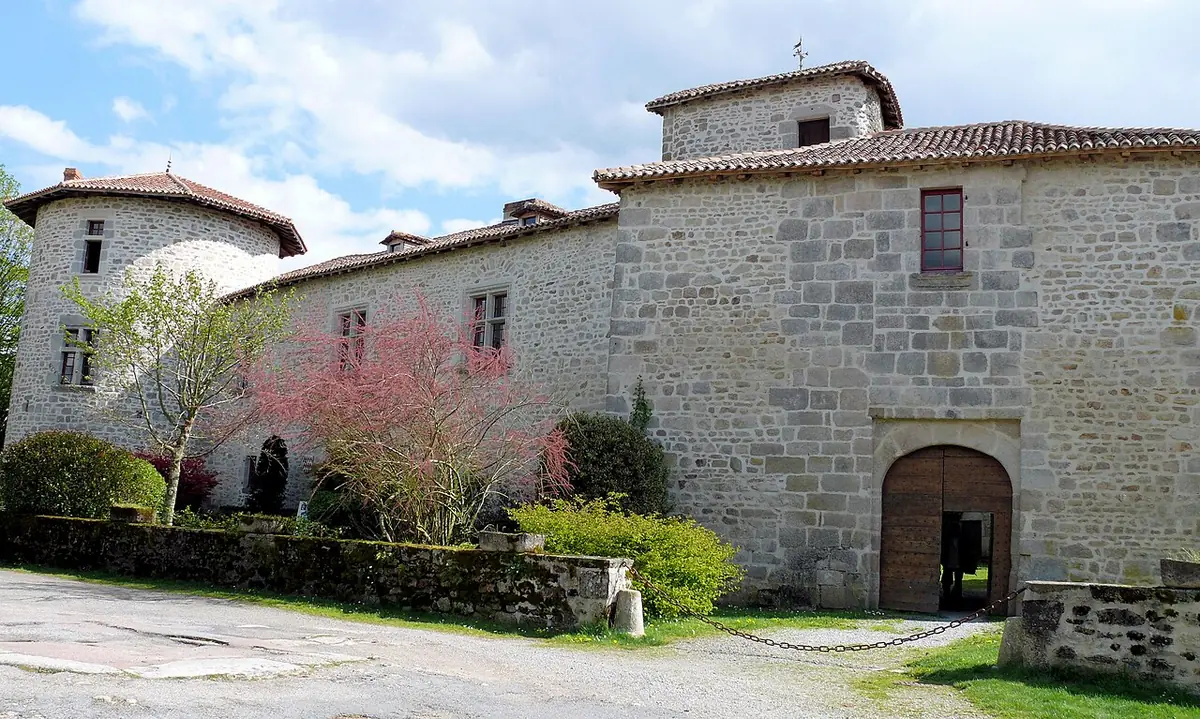 The stone castle at Mortemart with a round tower and a big arched doorway, behind a flowering tree
