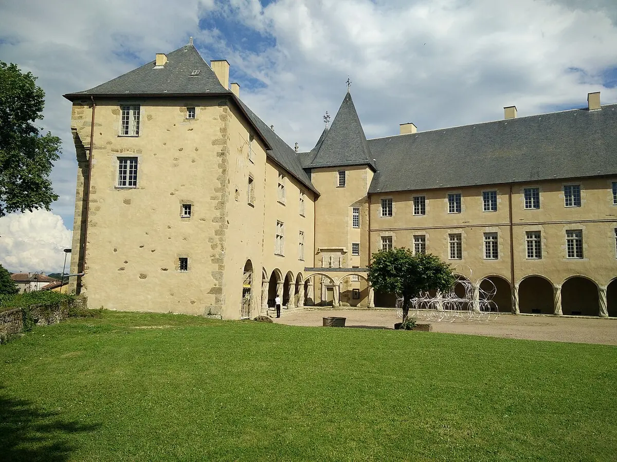 The courtyard of the Ch&acirc;teau de Rochechouart: pale stone wings with slate roofs and an arcade, around a lawn