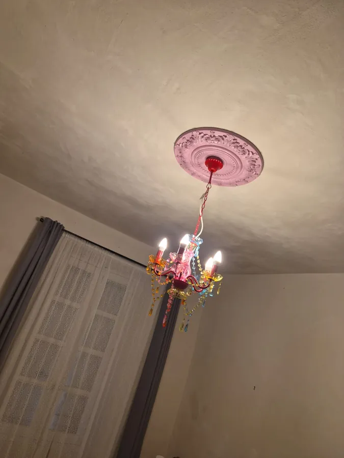 A colourful ornate chandelier hanging from a pink plaster ceiling rose
