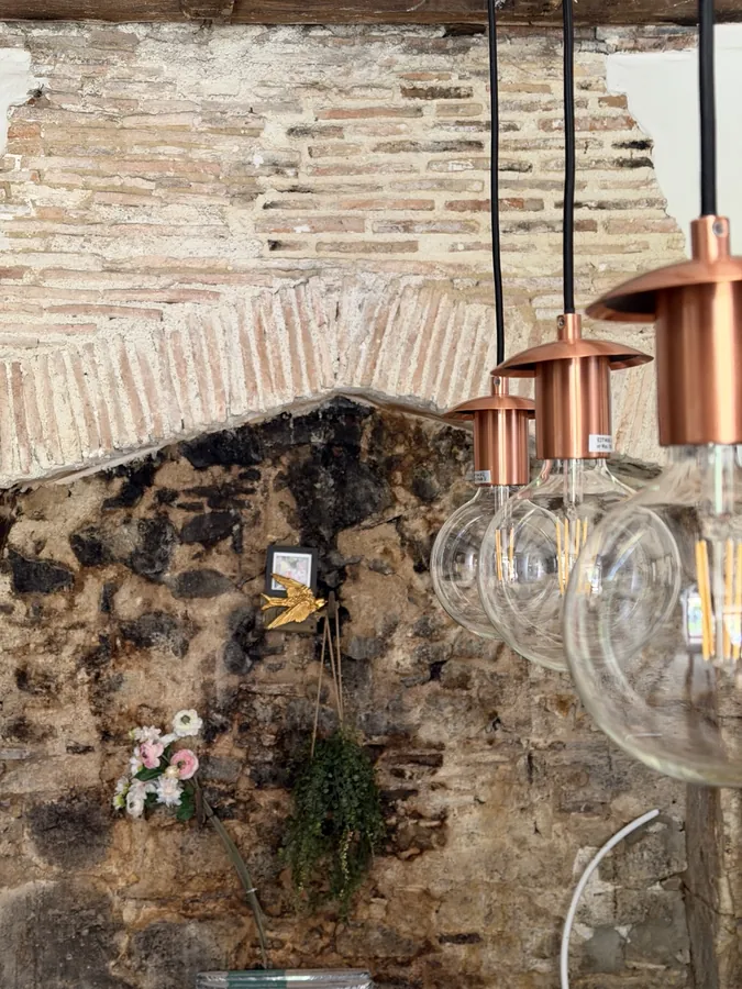 An old exposed stone and brick fireplace opening, with copper pendant lights and bare bulbs hanging in front of it