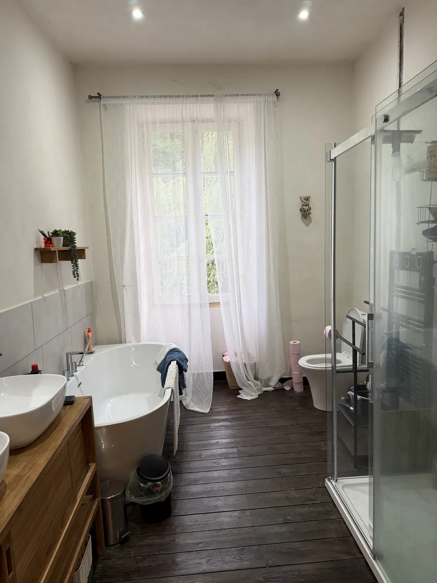 The main bathroom: a freestanding bath under a curtained window, twin basins on a wooden vanity and a large glass shower enclosure