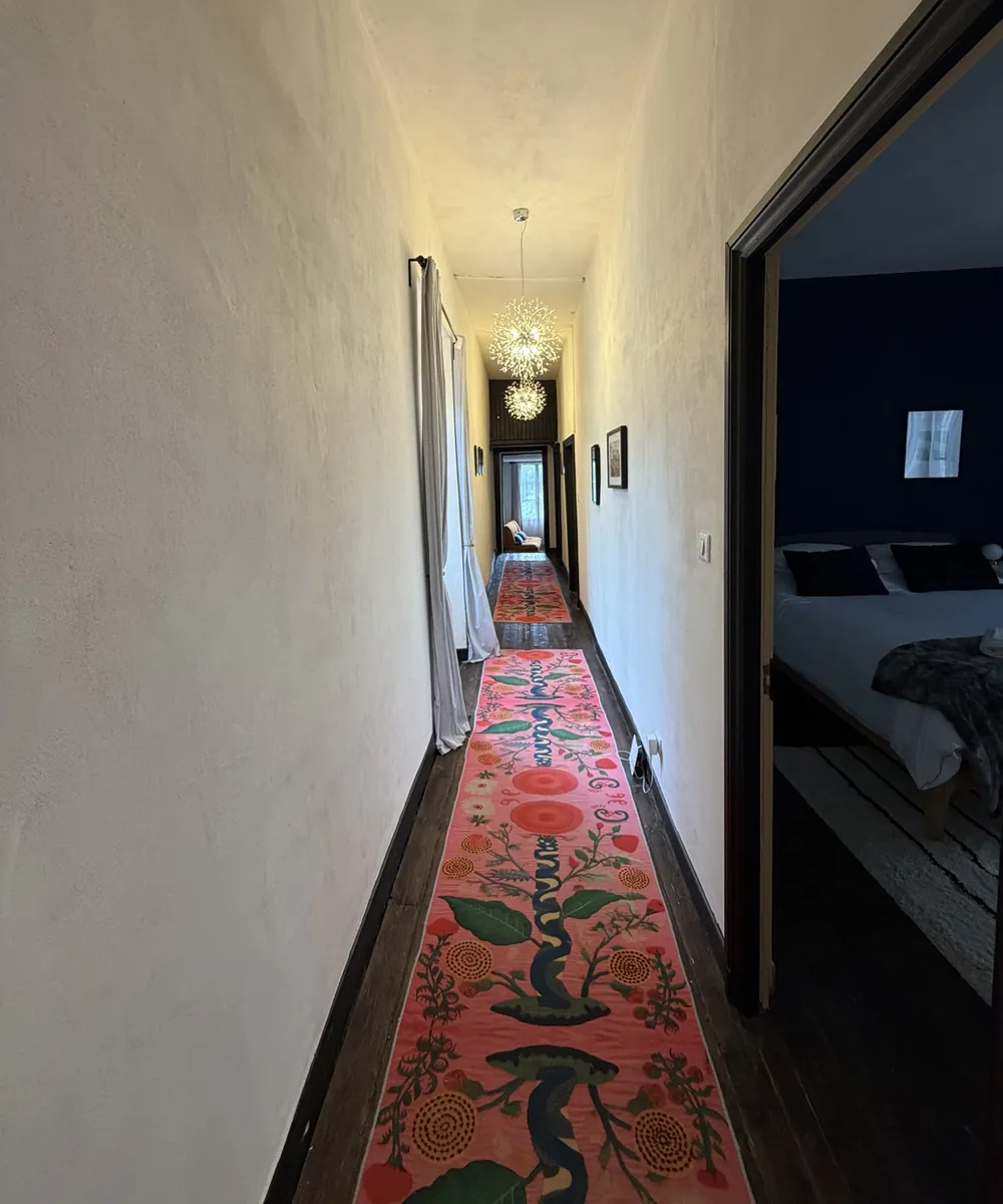The long upstairs hallway with dark original floorboards, a vivid floral runner down the middle and a pendant light at the far end