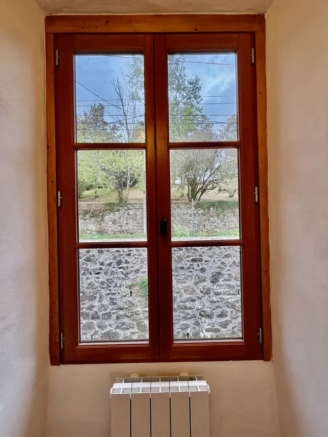 A wooden casement window looking out to trees and the higher road
