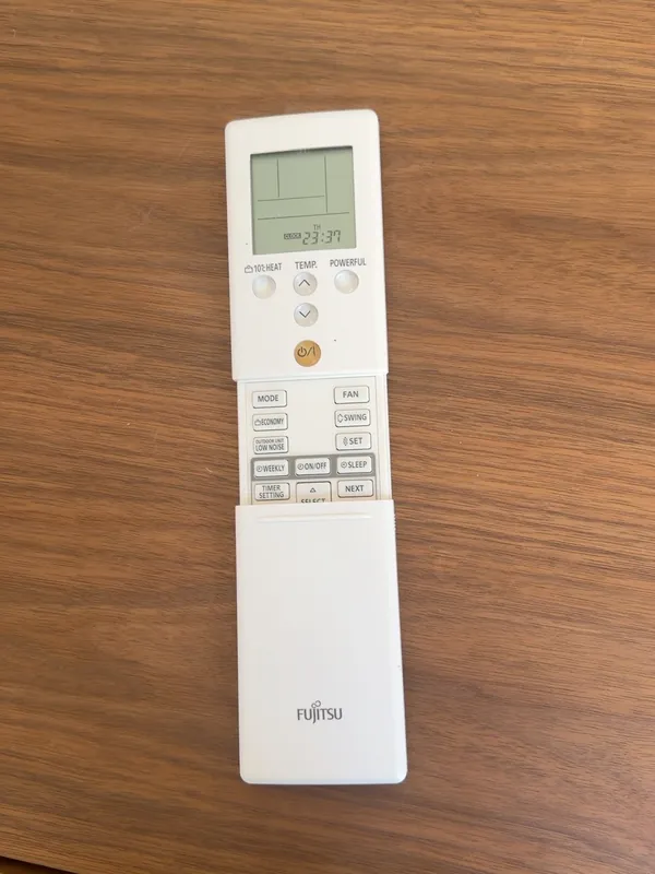 A white Fujitsu remote control lying on a wooden table, screen and buttons facing up