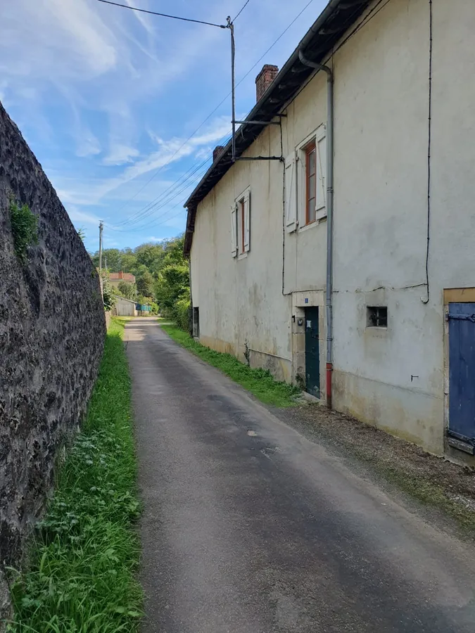 The lane running alongside the pale rendered wall of the house, with a high stone wall opposite