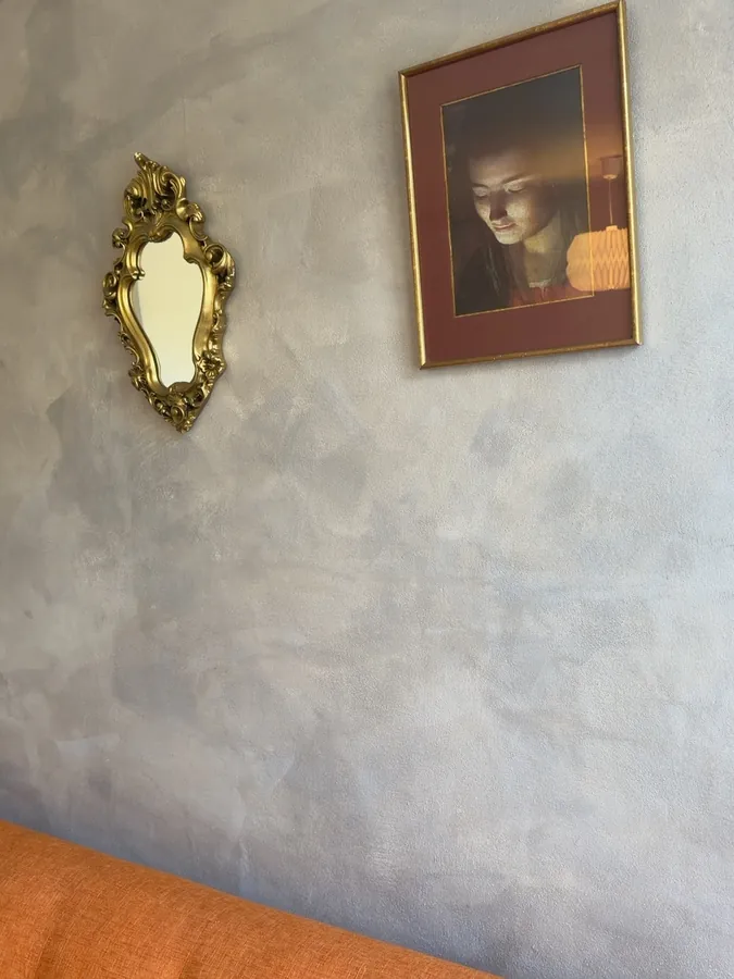 An ornate gilded mirror and a framed portrait hanging on a softly textured plaster wall