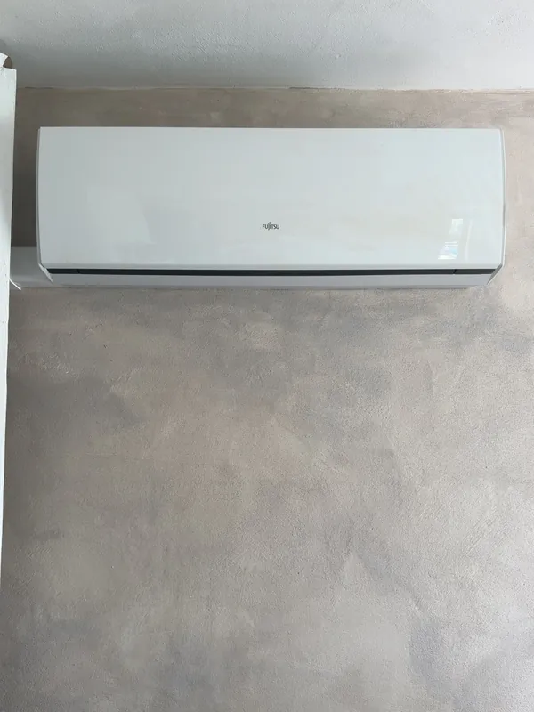 A white Fujitsu wall unit mounted high on a plain plastered wall