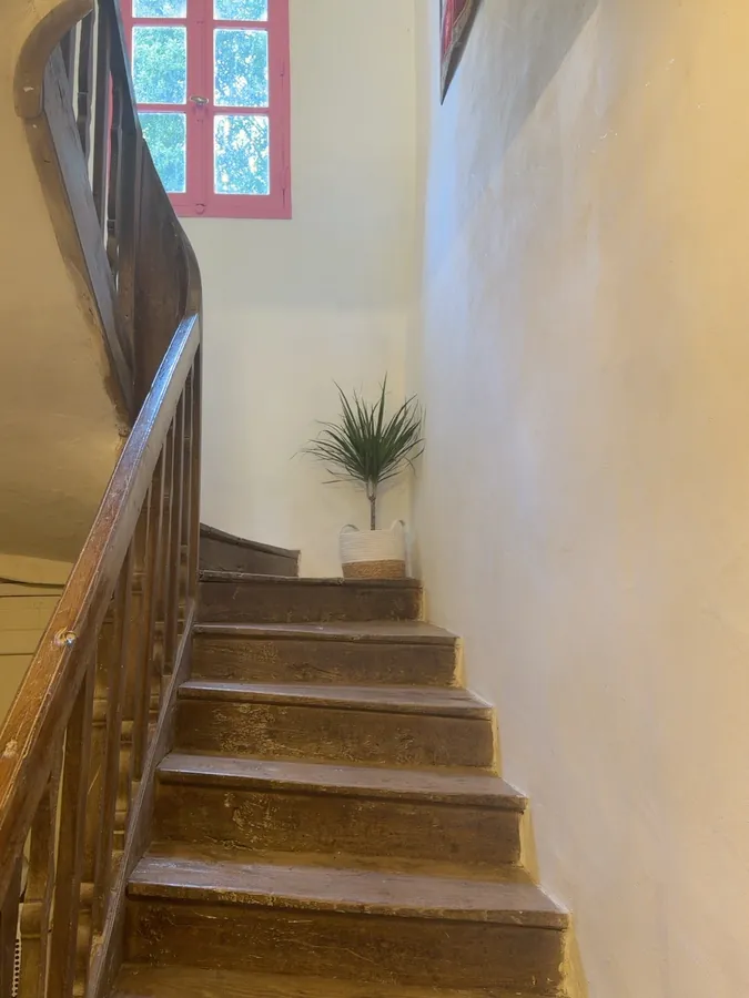 The original wooden staircase curving up towards a bright pink-framed window
