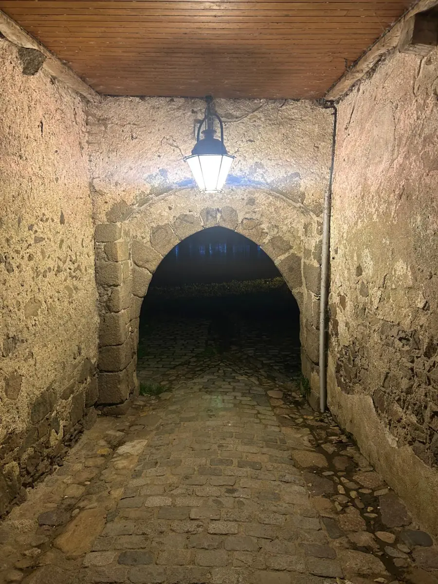A stone archway over a cobbled passage at night, lit by a single lantern