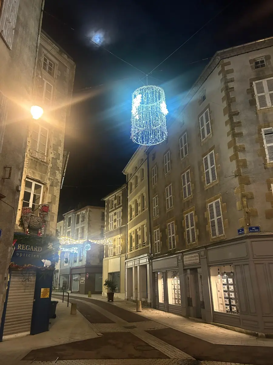 A town street at night with glowing Christmas light decorations strung above the road