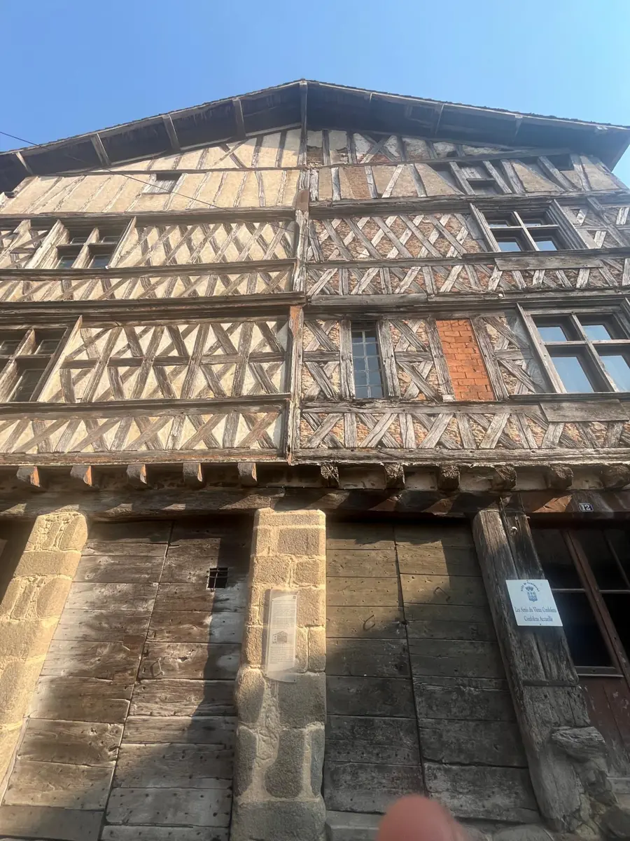 Looking up at a tall half-timbered house with a criss-cross pattern of dark beams, over old wooden shopfronts